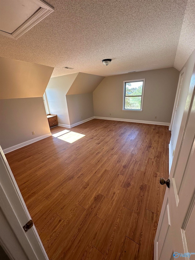 bonus room with lofted ceiling, wood-type flooring, and a textured ceiling