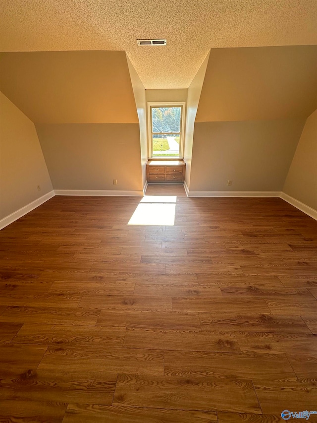 additional living space featuring a textured ceiling, lofted ceiling, and dark hardwood / wood-style floors