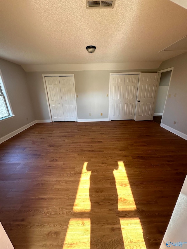 unfurnished bedroom featuring hardwood / wood-style flooring, a textured ceiling, and two closets