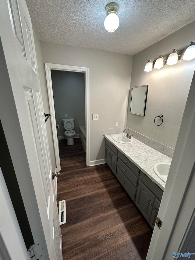 bathroom with hardwood / wood-style flooring, vanity, toilet, and a textured ceiling