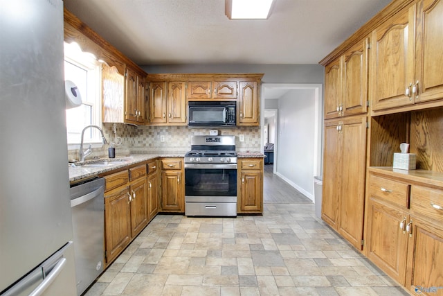 kitchen featuring a sink, stone finish flooring, appliances with stainless steel finishes, decorative backsplash, and light stone countertops