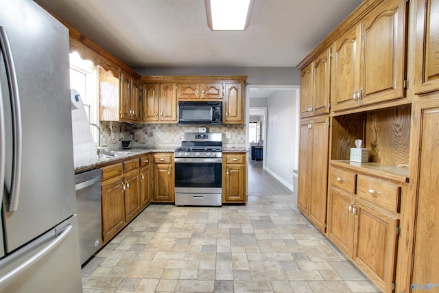 kitchen featuring brown cabinets, stone finish floor, stainless steel appliances, decorative backsplash, and light stone countertops