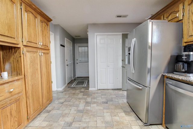 kitchen featuring brown cabinetry, visible vents, baseboards, stainless steel appliances, and stone finish floor