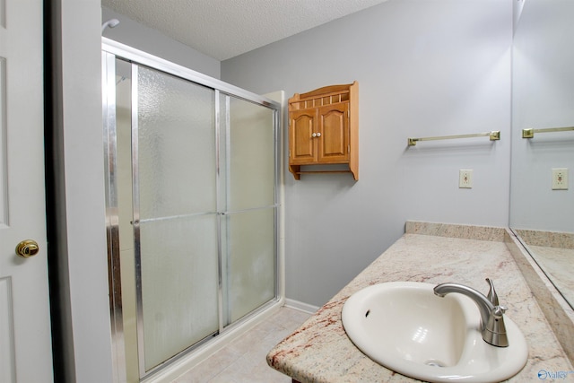 full bath featuring tile patterned floors, a stall shower, a textured ceiling, baseboards, and vanity