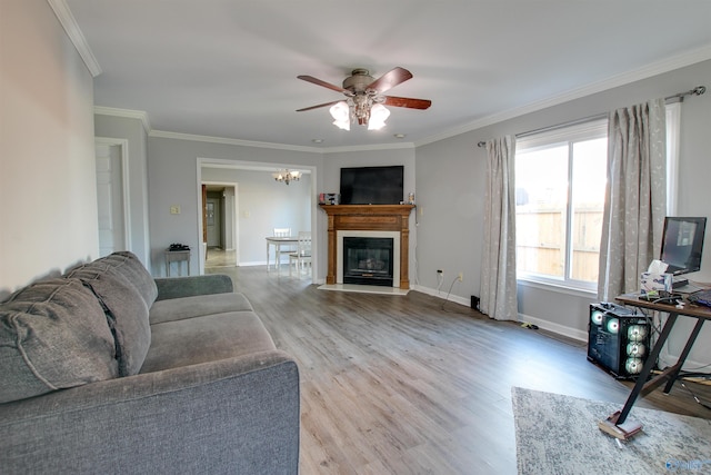 living room with baseboards, ornamental molding, ceiling fan with notable chandelier, wood finished floors, and a glass covered fireplace