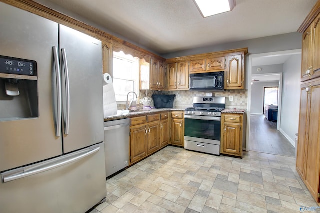 kitchen with light stone counters, a sink, decorative backsplash, stainless steel appliances, and brown cabinets