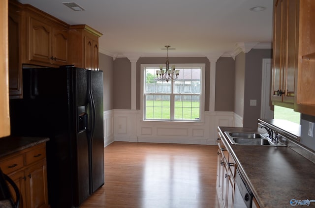 kitchen with a sink, black fridge, ornate columns, dark countertops, and wainscoting