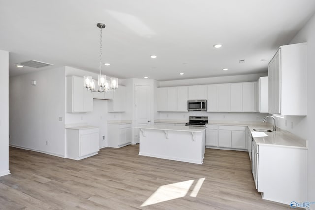 kitchen with a kitchen island, appliances with stainless steel finishes, white cabinetry, hanging light fixtures, and light wood-type flooring