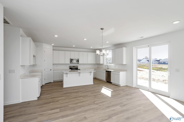 kitchen featuring pendant lighting, white cabinetry, a center island, stainless steel appliances, and light hardwood / wood-style flooring