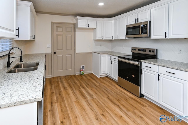 kitchen with stainless steel appliances, decorative backsplash, light wood-style floors, white cabinets, and a sink