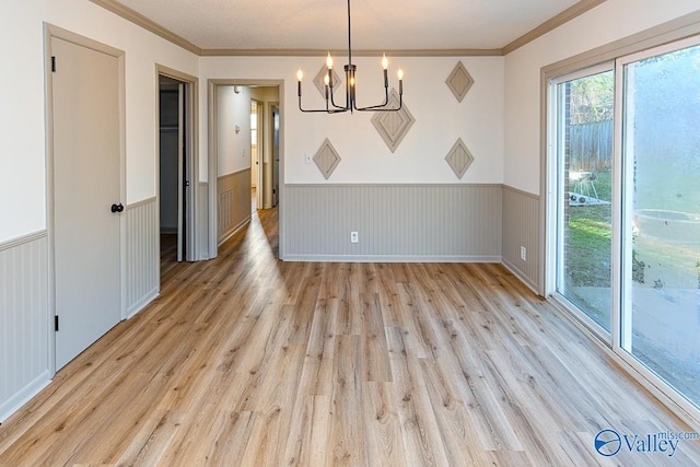 unfurnished dining area with light wood-style flooring, a chandelier, ornamental molding, and wainscoting