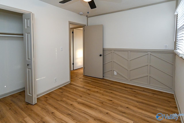 unfurnished bedroom with a wainscoted wall, a closet, a decorative wall, a ceiling fan, and wood finished floors