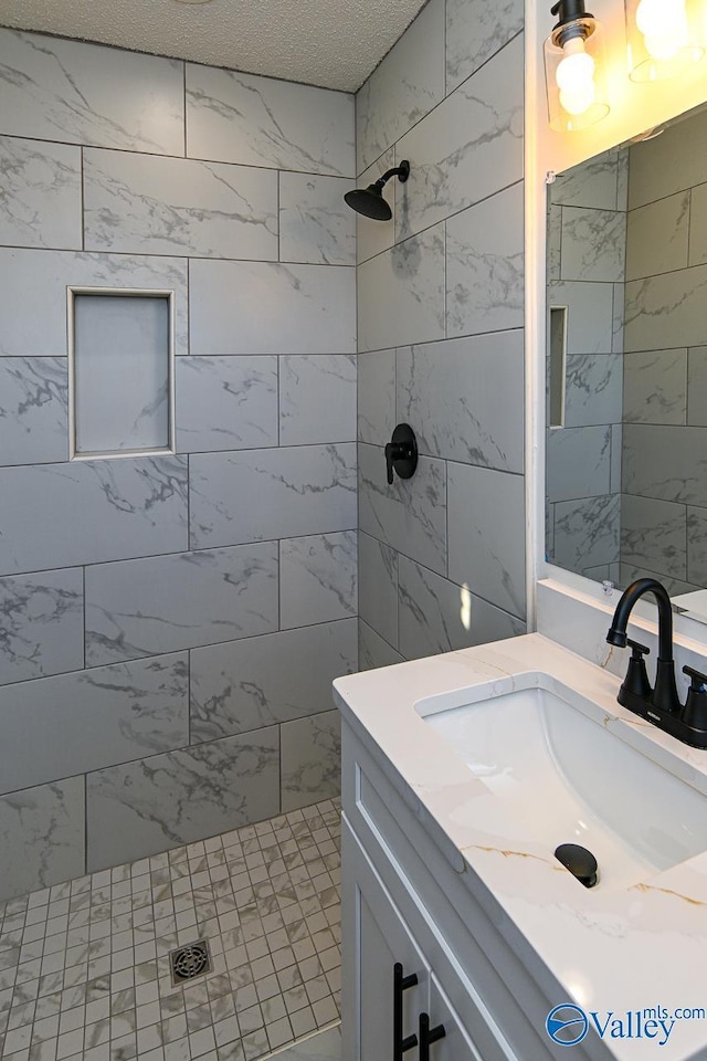 bathroom with a textured ceiling, tiled shower, and vanity