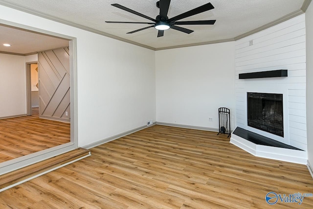 unfurnished living room with a textured ceiling, a fireplace, crown molding, and wood finished floors