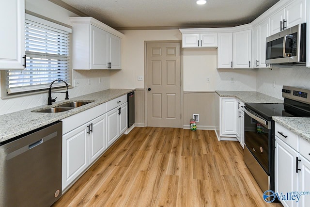 kitchen with decorative backsplash, light wood-style flooring, stainless steel appliances, white cabinetry, and a sink