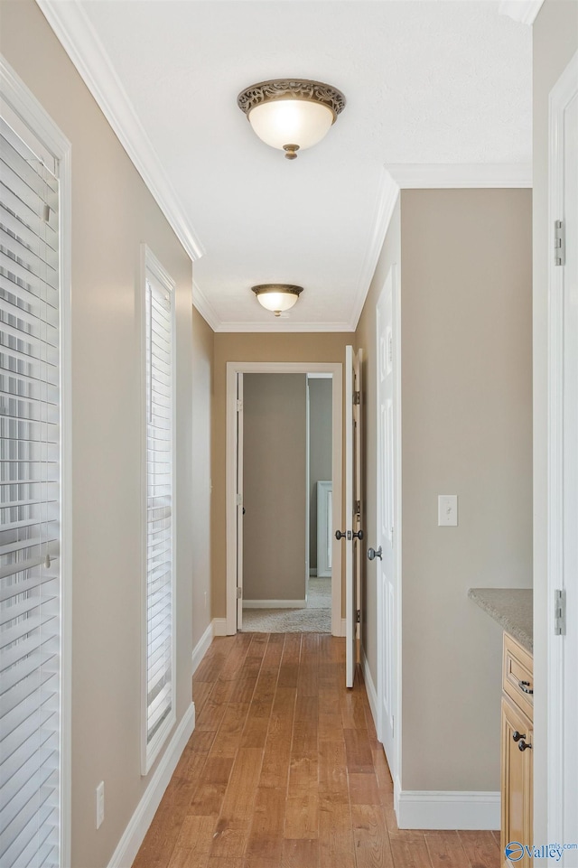 hallway with ornamental molding, baseboards, and light wood finished floors