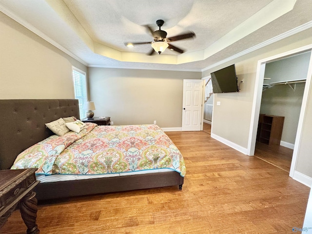 bedroom with baseboards, a textured ceiling, light wood-type flooring, and a raised ceiling