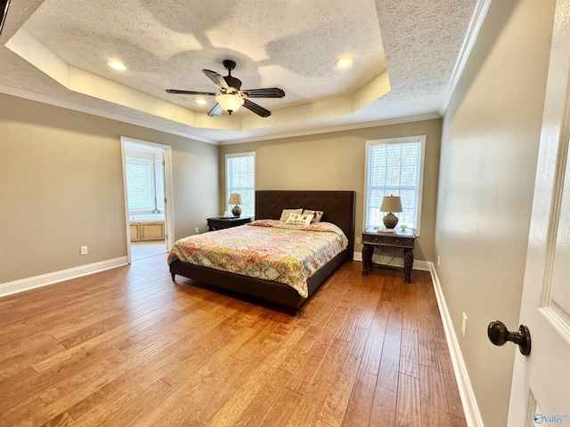 bedroom featuring a raised ceiling, crown molding, and light wood-style floors
