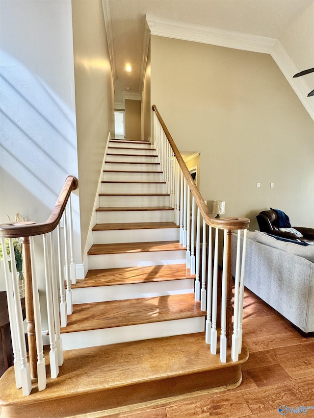 staircase with lofted ceiling, ornamental molding, and wood finished floors