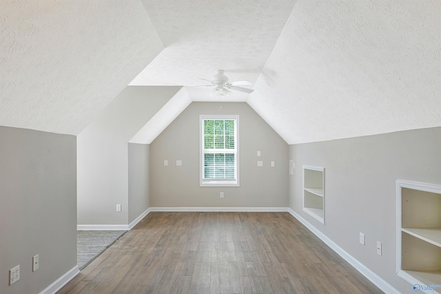 bonus room with a textured ceiling, built in shelves, ceiling fan, and wood finished floors