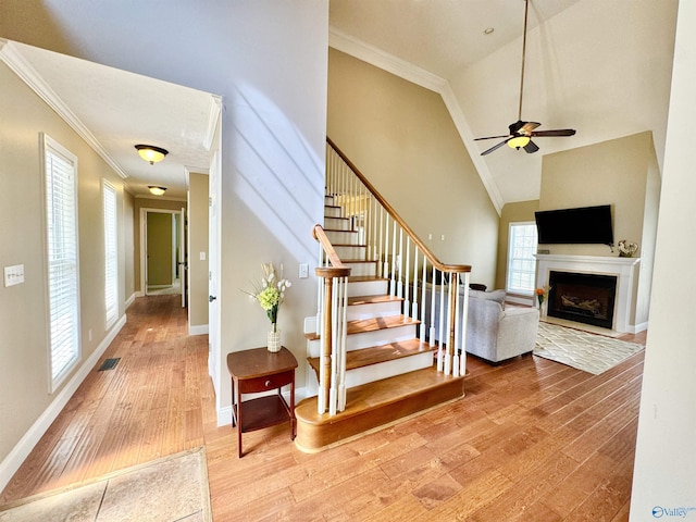 staircase featuring a fireplace, ceiling fan, wood finished floors, and crown molding