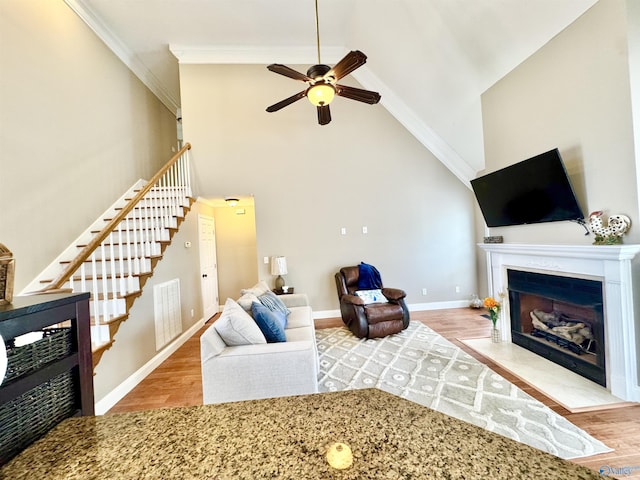living area featuring a ceiling fan, a fireplace with flush hearth, stairway, and wood finished floors