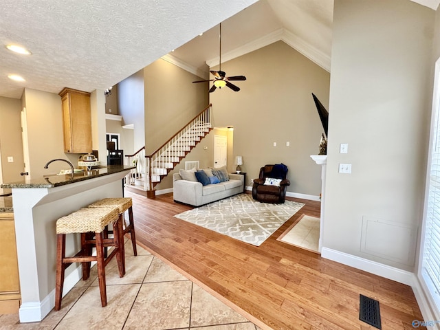 living room with a textured ceiling, visible vents, light wood finished floors, stairs, and ceiling fan