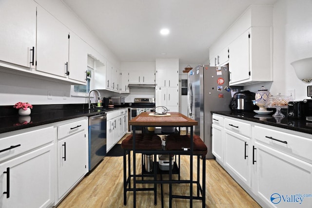 kitchen with light wood-style floors, white cabinetry, appliances with stainless steel finishes, under cabinet range hood, and a sink
