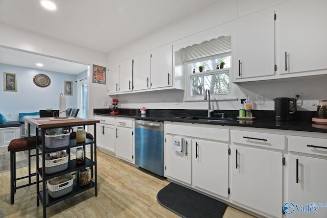 kitchen with white cabinetry, dark countertops, light wood-style floors, stainless steel dishwasher, and a sink
