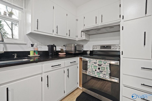 kitchen featuring white cabinets, a sink, dark countertops, under cabinet range hood, and double oven range