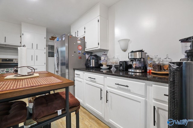 kitchen with light wood-style flooring, white cabinetry, under cabinet range hood, dark stone counters, and stainless steel appliances