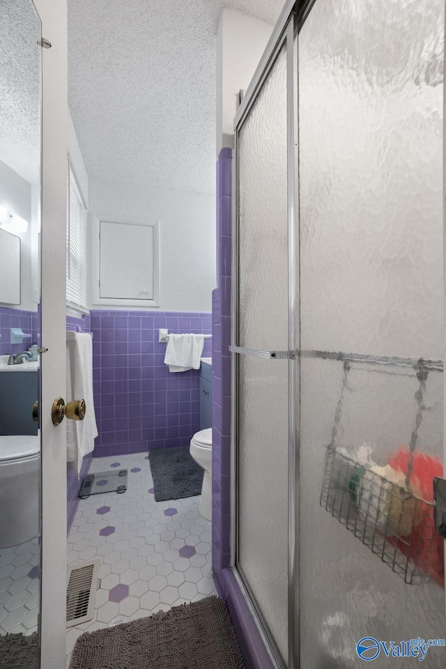bathroom featuring toilet, a textured ceiling, a shower stall, and tile patterned flooring