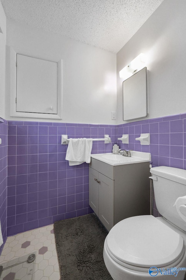 bathroom featuring vanity, a textured ceiling, toilet, a wainscoted wall, and tile walls