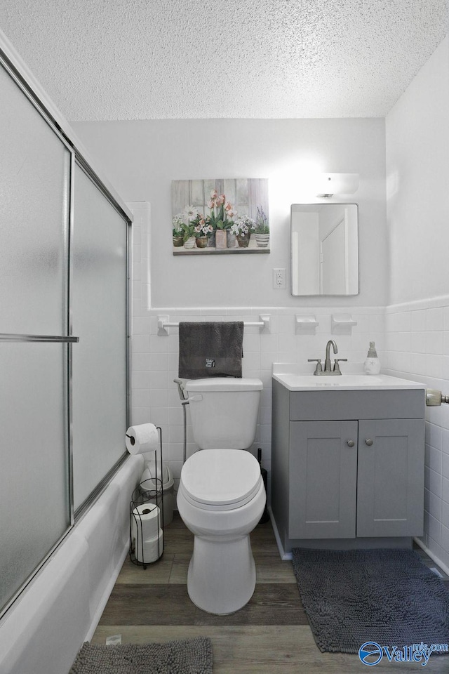 bathroom with toilet, a textured ceiling, wood finished floors, and shower / bath combination with glass door