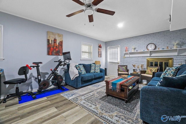 living area featuring wood finished floors, ornamental molding, brick wall, and a ceiling fan