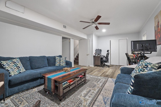living area featuring wood finished floors, a ceiling fan, visible vents, and stairs