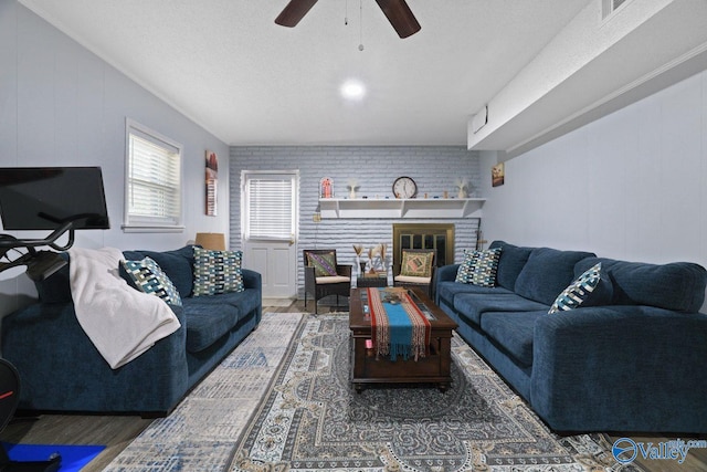 living area with brick wall, visible vents, ceiling fan, and wood finished floors