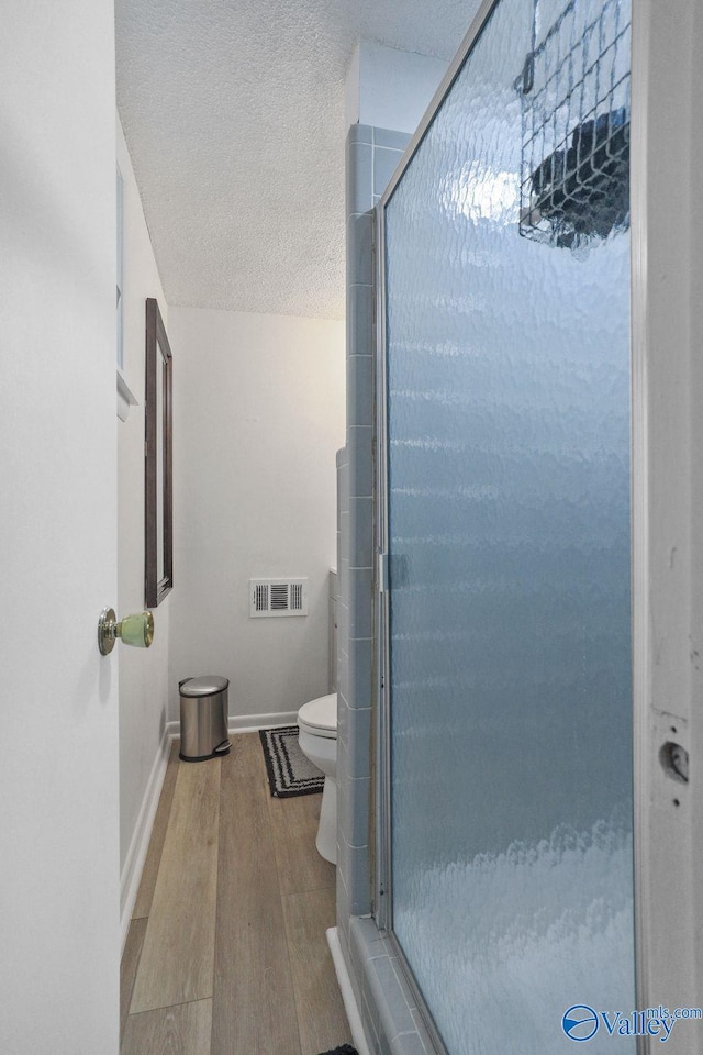 bathroom featuring visible vents, baseboards, a textured ceiling, a shower stall, and wood finished floors