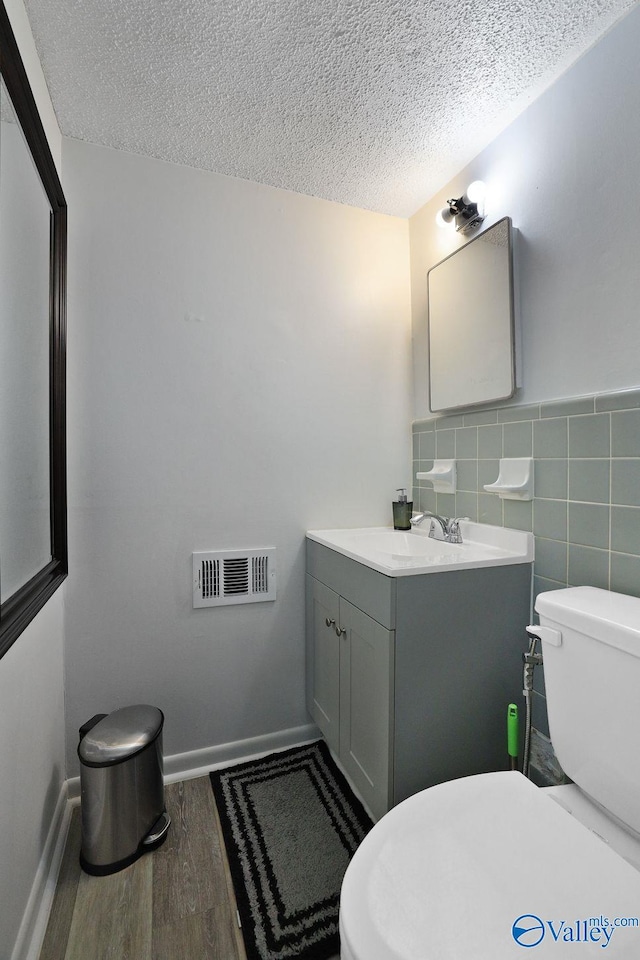 half bath with visible vents, toilet, tile walls, a textured ceiling, and wood finished floors