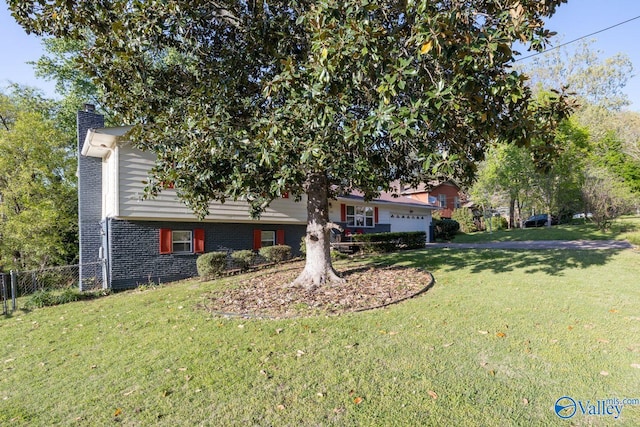 tri-level home with a garage, fence, a chimney, and a front lawn