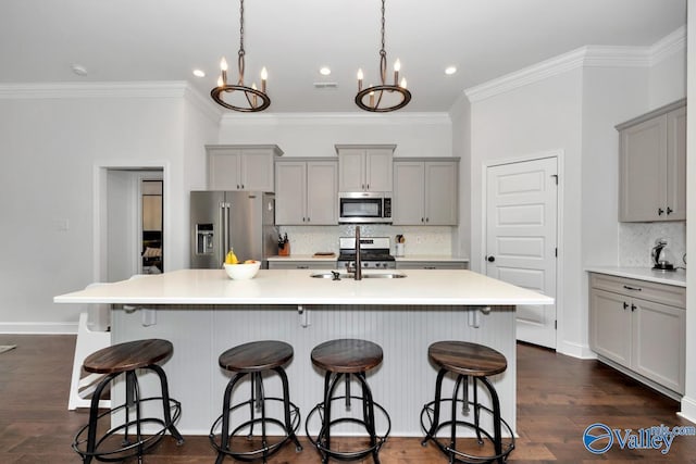 kitchen featuring an island with sink, dark wood-style floors, stainless steel appliances, gray cabinetry, and a sink