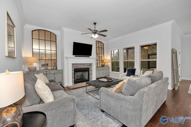 living room featuring baseboards, a stone fireplace, dark wood finished floors, and crown molding