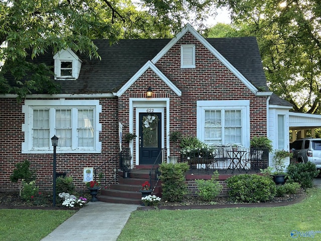 view of front of home with brick siding, a front lawn, and roof with shingles