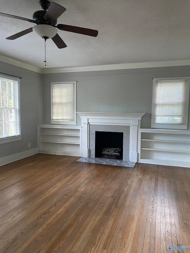 unfurnished living room with hardwood / wood-style flooring, ornamental molding, ceiling fan, a textured ceiling, and a brick fireplace