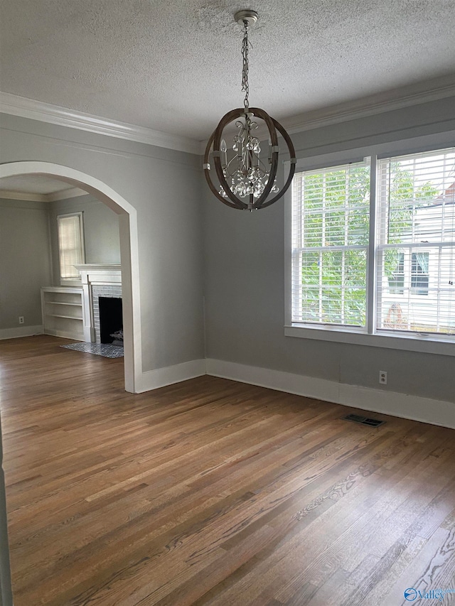 unfurnished dining area with ornamental molding, dark wood-type flooring, a textured ceiling, and a notable chandelier