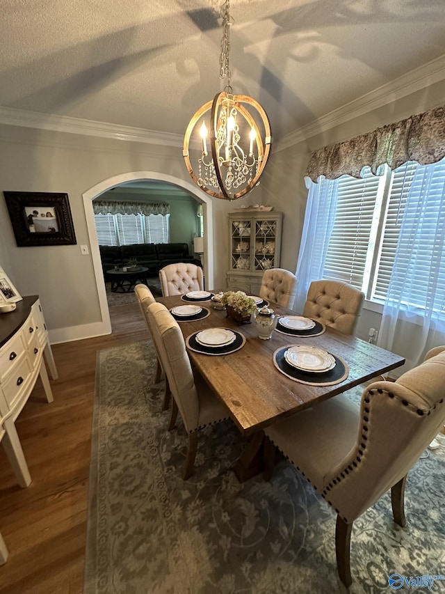 dining room featuring an inviting chandelier, a textured ceiling, ornamental molding, arched walkways, and wood finished floors