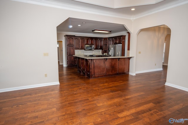 kitchen with decorative backsplash, dark wood-style floors, a peninsula, arched walkways, and stainless steel appliances