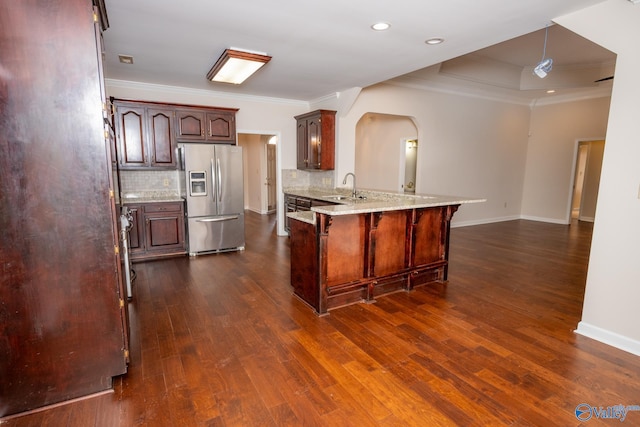 kitchen featuring a kitchen bar, a peninsula, stainless steel refrigerator with ice dispenser, arched walkways, and a sink