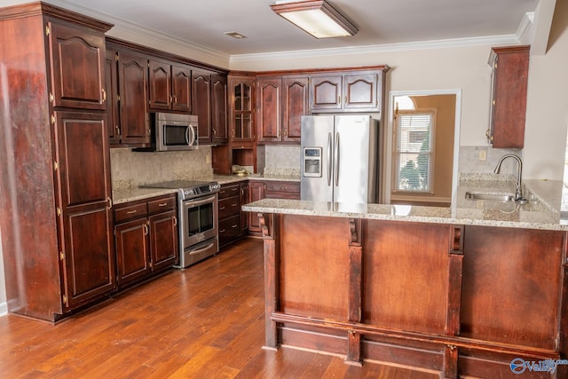 kitchen with ornamental molding, a sink, light stone counters, appliances with stainless steel finishes, and a peninsula