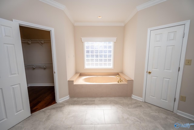 bathroom featuring a bath, a walk in closet, baseboards, and ornamental molding